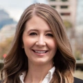 Whitney Knuf Ahn, Vice President, Nashville Cost Centre Leader, standing outside featuring an urban cityscape with tall buildings and a mix of architectural styles. The scene includes some trees with autumn foliage, adding a touch of color.