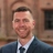 Portrait of Mark Ferguson, Associate, UK, standing against brown building in blue suit.