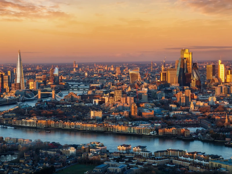 Panoramic, elevated view of the urban London skyline with soft, golden sunlight during sunrise, England