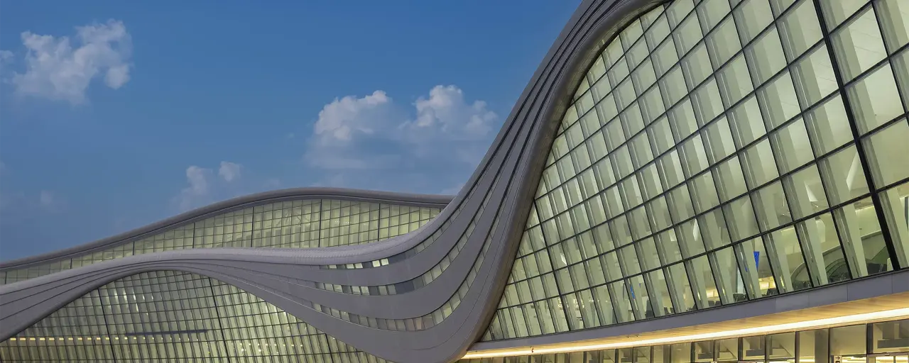 The exterior of Zayed International Airport, a glass front airport terminal against a blue evening sky 