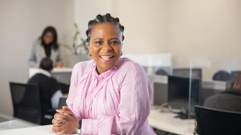 Portrait of Babalwa Damane, Director, Mining and Metals, South Africa sitting in office space in pink shirt smiling.