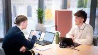 Two employees smiling at their desk, in a meeting