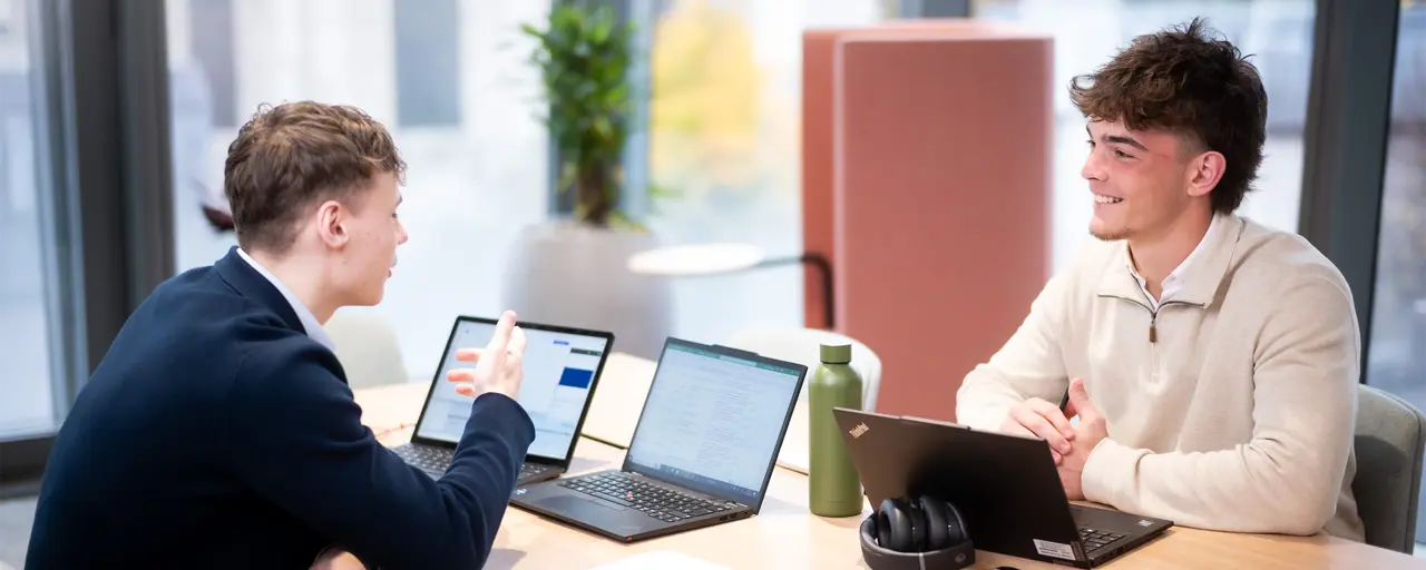 Two employees smiling at their desk, in a meeting