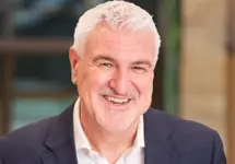 Steve Perkins, Director, outside in front of a blurred brown background featuring a building and mix of natural and urban elements.