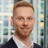 Portrait of Matt Lowe, Principal Consultant, with city landscape featuring building with lots of windows in the background.