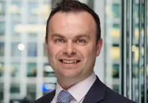 Portrait of Chris Swann, Associate Director, Advisory and Consulting, with city landscape featuring building with lots of windows in the background.