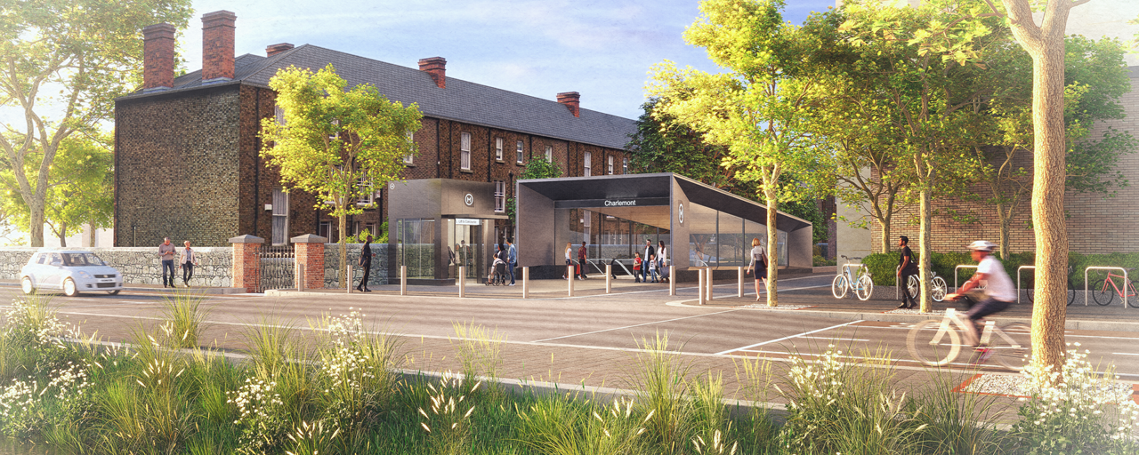 The entrance to a modern metro station, next to brickwork buildings and with a background of trees. 