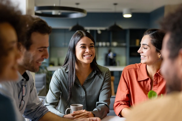 Group of colleagues sitting together having a conversation, gathered around a table with coffee mugs.