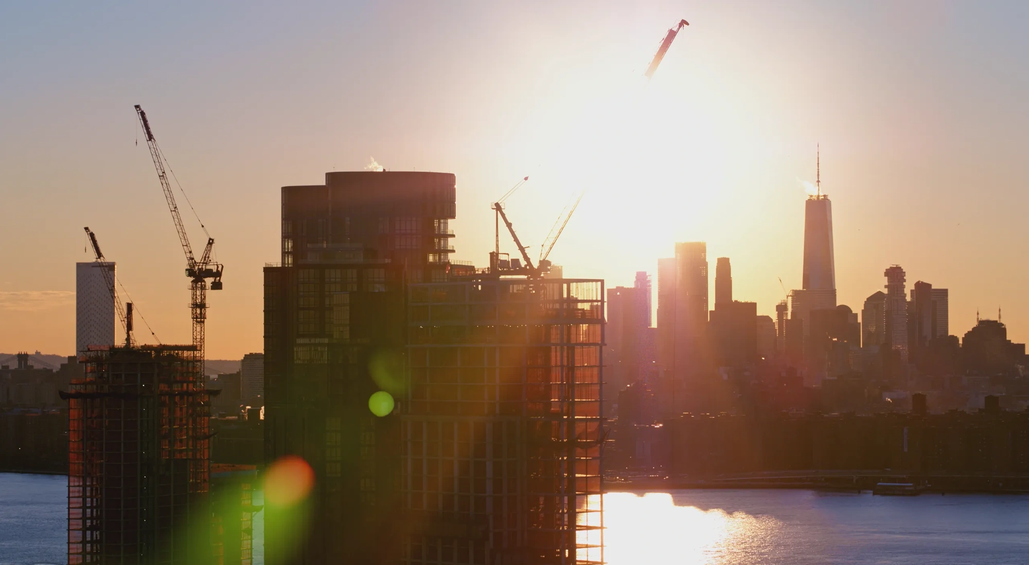 New residential towers' construction on the waterfront in Brooklyn, with the scenic view of Manhattan skyline, at sunset.