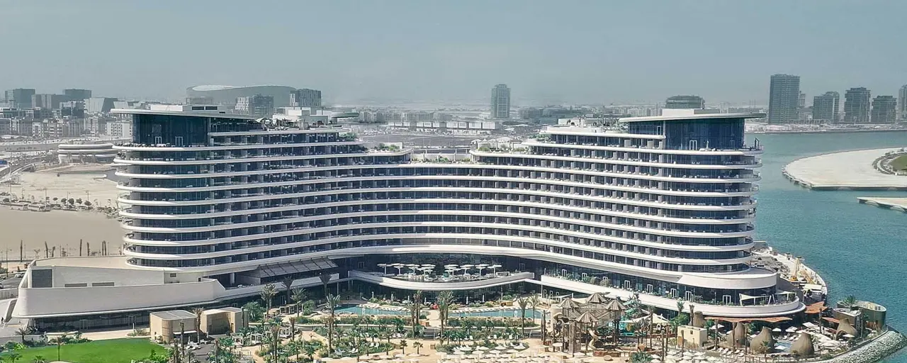 A beach front multi-story hotel resort complex with sun loungers and the sea in the foreground. 