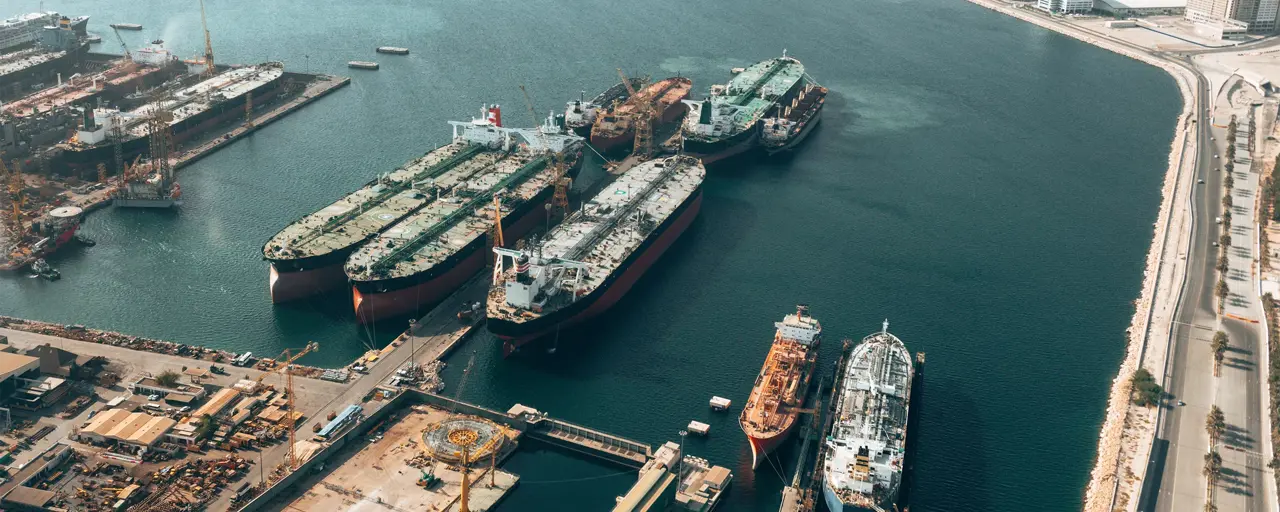 Image of maritime boats pulling up to harbor, with blue sea.