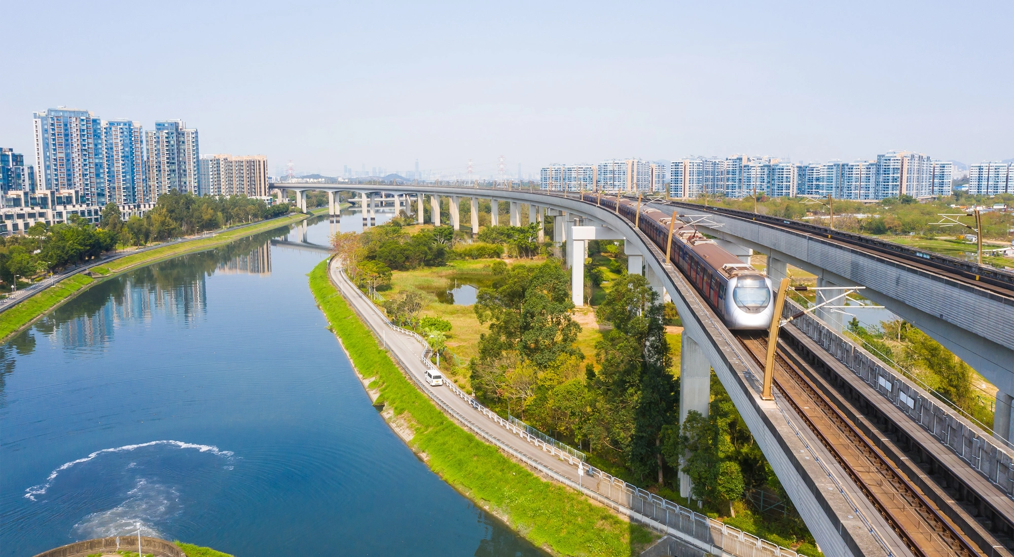 Picture of train going over water stream and fields with city in the background.