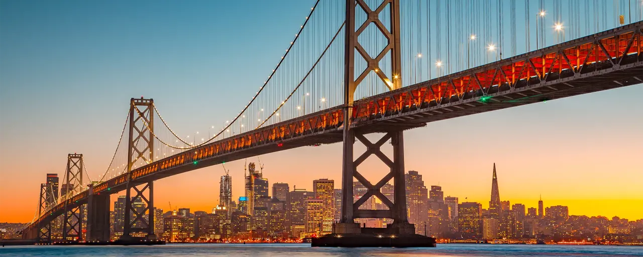 Panoramic view of San Francisco skyline with famous Oakland Bay Bridge illuminated in beautiful golden evening light at sunset in summer