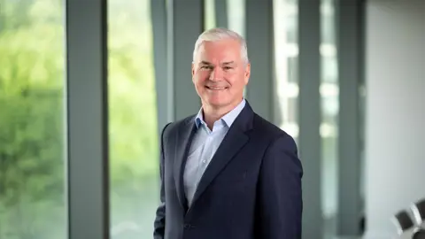 Vincent Clancy, CEO, smiling in front of a window with trees behind him