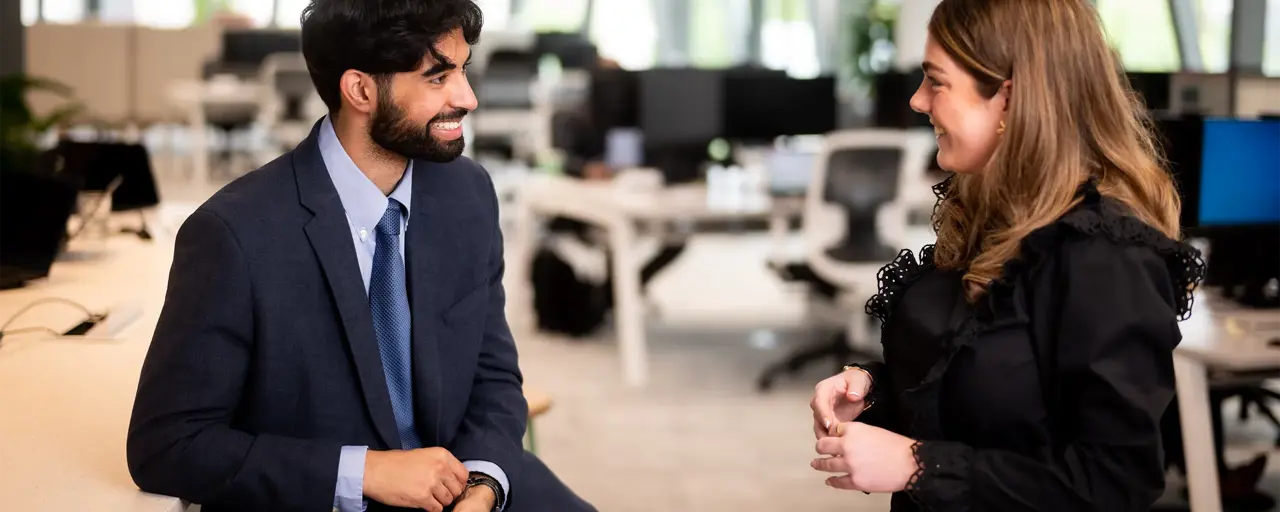 Two young employees having a casual chat in office space, smiling.