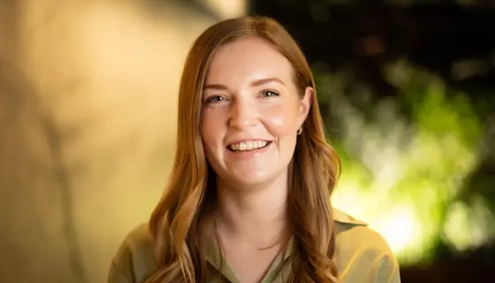 Portrait of Katie Demack, Senior Project Manager, Australia, close up wearing green shirt with greenery in background.