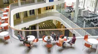 Furniture in open plan building with modern staircase and college students meeting friends.