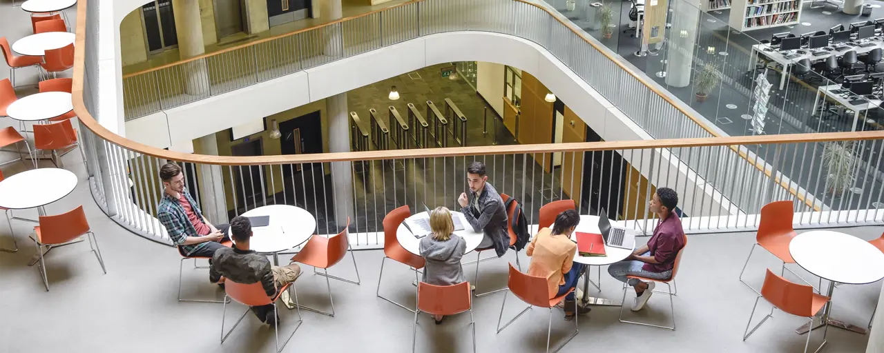 Furniture in open plan building with modern staircase and college students meeting friends.