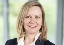 Patricia Moore, Managing Director, UK, standing in office space in front of a glass window. There are hints of greenery, suggesting some trees or plants.