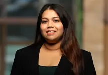 Portrait of Dionne Pereira, Senior Sustainability Consultant, outside in front of a blurred brown background featuring a building and mix of natural and urban elements.