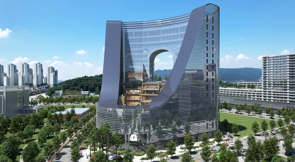 Modern curved glass building with a large central arch, surrounded by greenary and nearby city buildings.
