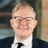 Ben Carter, Principal Consultant, UK, outside in front of a blurred brown background featuring a building and mix of natural and urban elements.