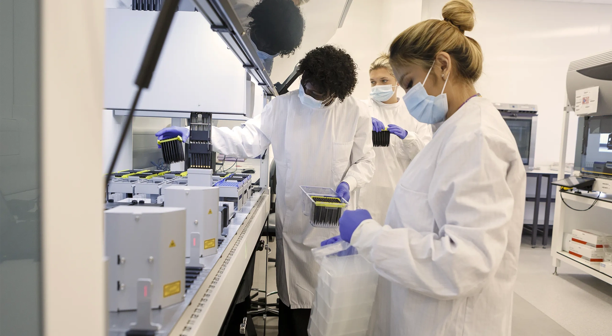 Students in a university science lab with white coats and face masks on working on machine.