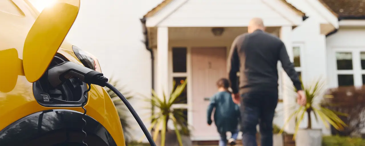 Yellow car being charged in driveway while a man and boy enter the house