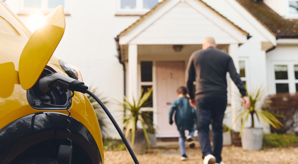 Yellow car being charged in driveway while a man and boy enter the house