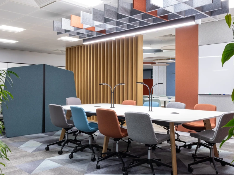 Turner & Townsend Bristol office. Plants in each corner with a meeting bank in the centre. There's colorful chairs around the table and a orange panel behind.