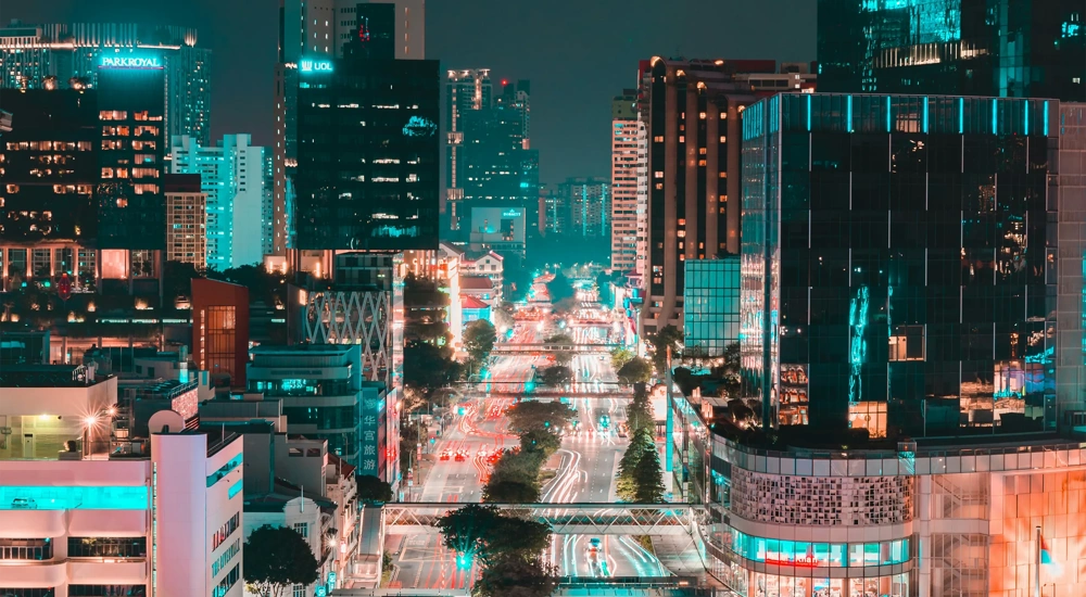 Singapore at night with glass skyscraper buildings and brightly lit roads with traffic