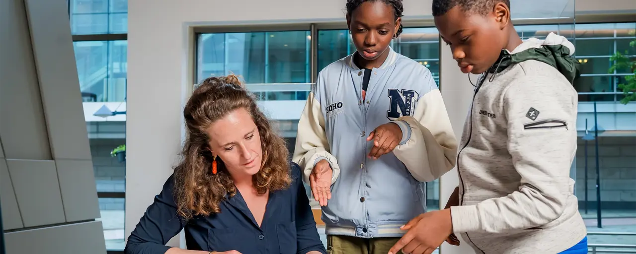 Two young people and a woman looking at information on a desk