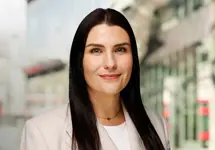 Portrait of Tiffany Emmett, Associate Director, Construction Economics, standing outside in front of buildings featuring an urban cityscape with a mix of architectural styles. The scene includes some windows and red features, adding a touch of color.