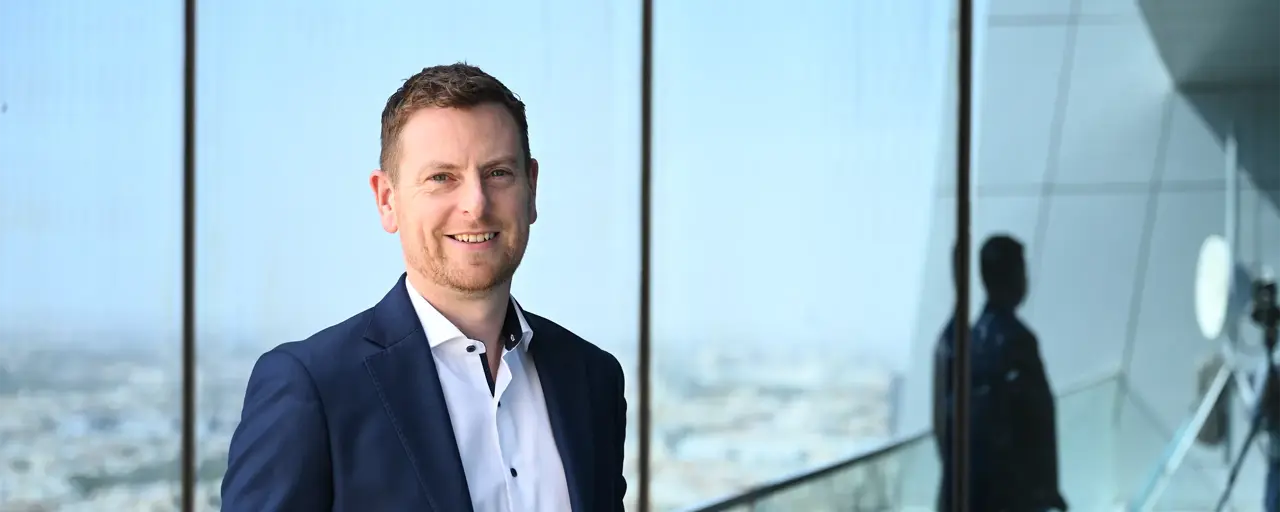 Alan Coary, Middle East data centre lead business suit standing on a balcony or near a large window, with a cityscape visible in the background.