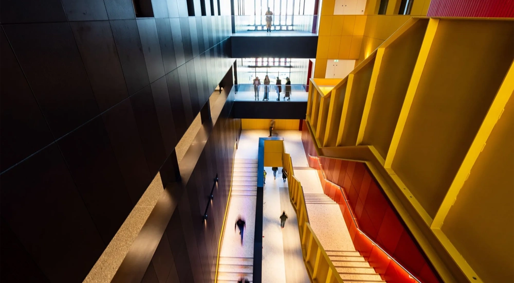Yellow and red staircase in a black building with people chatting and walking down.