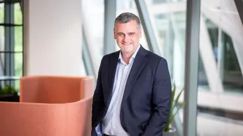 Chris Sargent, UK Managing Director, Real Estate, smiling in an office with orange walls and large glass windows