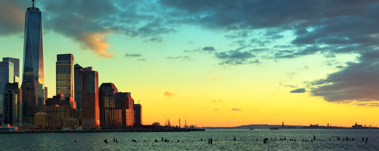 Skyline photo of New York City with skyscraper buildings on the left of the photo and water in the foreground