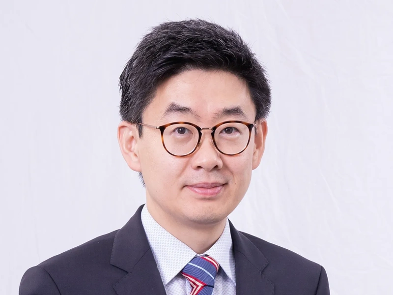 Portrait of Yan Zhou, Director of Energy and Infrastructure, Greater China, smiling in blue suit against white backdrop.