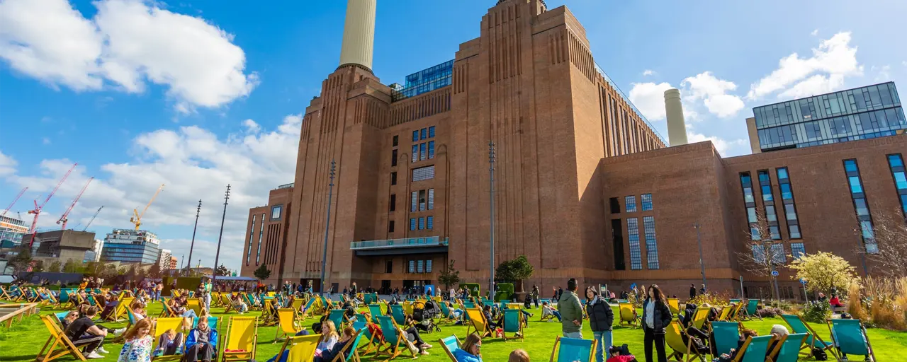 Group of people sitting outside in deck chairs in front of Battersea Power Station on a sunny day