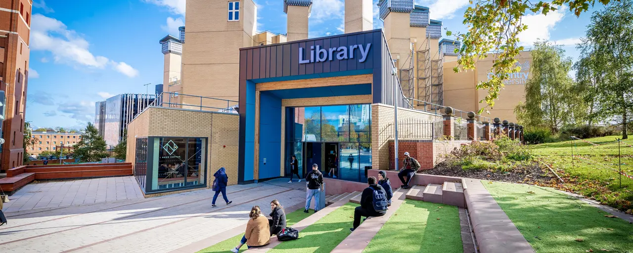 Students sitting on a lawn and stairs outside a library building