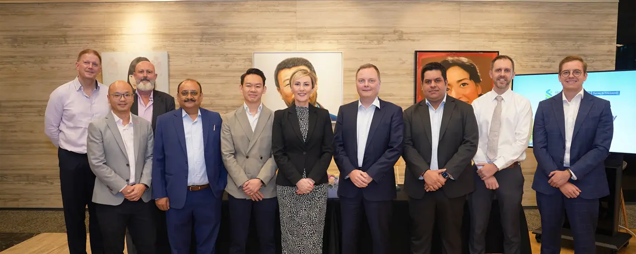 Group of ten colleagues standing for a photo, smiling. There are nine males and a female colleague in the middle. There are also pieces of artwork hanging in the back.