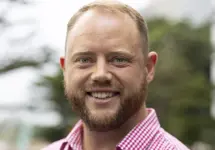 Liam Bray, Director, Portfolio Management, standing outside. There are hints of greenery, suggesting some trees or plants.