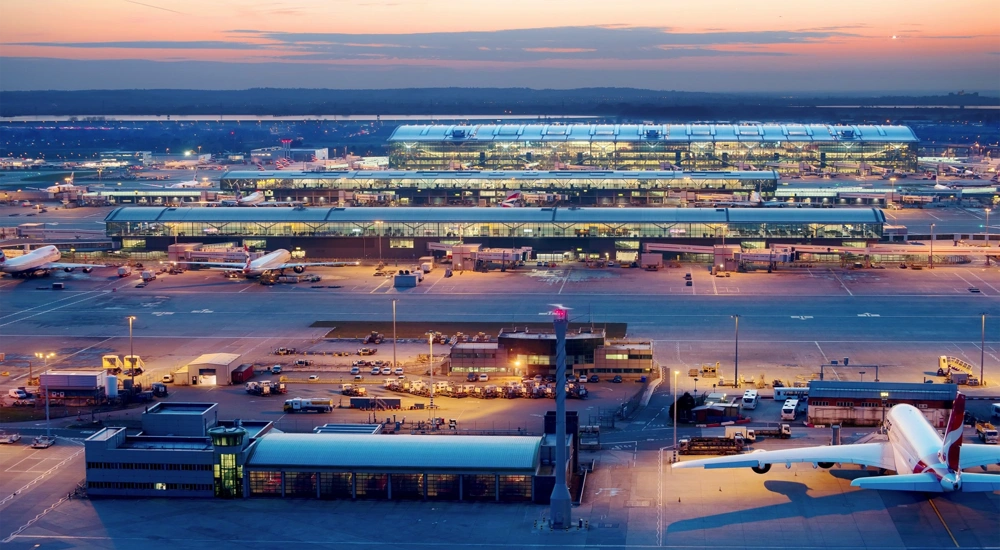 Heathrow airport featuring an airplane, bright lights in the building and orange sunset in the background