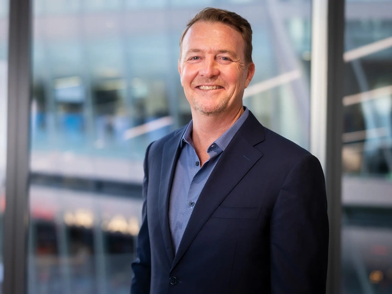 Portrait of Tim White, Regional Managing Director, Africa, standing in from of windows in office in blue suit, smiling.