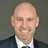 Portrait of Mark Utting, Managing Director, Switzerland, smiling in a suit against dark grey background.