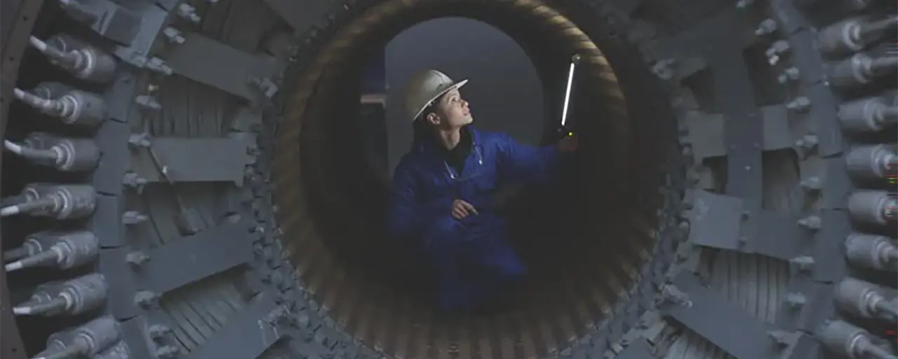 Photo of woman in blue construction wear and white helmet standing inside machine