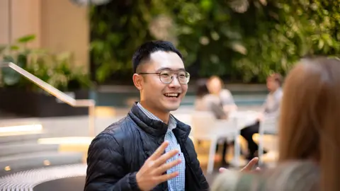 Male colleague in glasses, in a plant-filled office, smiling while talking