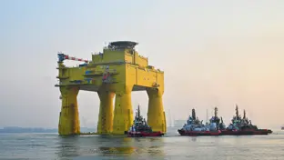 The DolWin epsilon converter station (an solid, yellow structure) floating in the sea.  