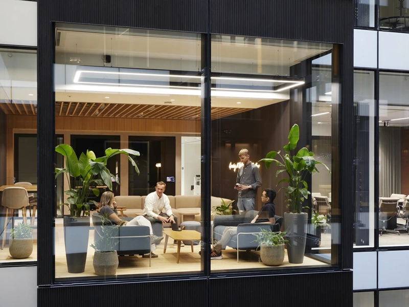 Modern office lounge with green booth seating, large windows and people working and meeting.