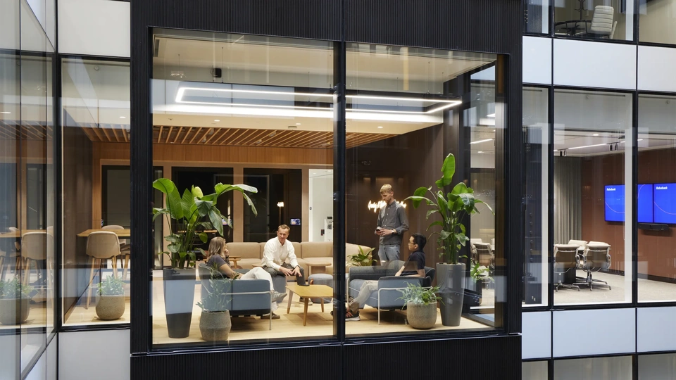 Modern office lounge with green booth seating, large windows and people working and meeting.
